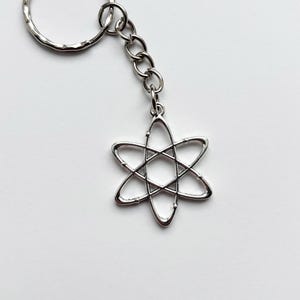 Może przedstawiać: Srebrny brelok do kluczy z sześcioramiennym wzorem gwiazdy, połączony z łańcuchem i teksturowanym k&oacute;łkiem na klucze. Brelok wykonany jest z błyszczącego metalu na gładkim białym tle.