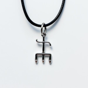 Puede incluir: Collar con colgante plateado y cordón negro. El colgante tiene un diseño de tridente con tres puntas rojas. El collar se muestra sobre un fondo blanco.