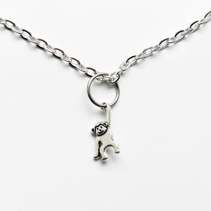 Peut inclure: Un collier argenté avec une chaîne et un petit pendentif singe. Le pendentif singe est suspendu à un anneau fixé à la chaîne. Le fond est blanc.