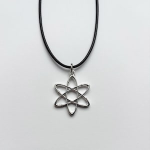 以下が含まれることがあります： 銀色の原子ペンダントネックレス。ペンダントは、六芒星の形をした原子モデルです。ネックレスは黒いコードで、白い背景にセットされています。