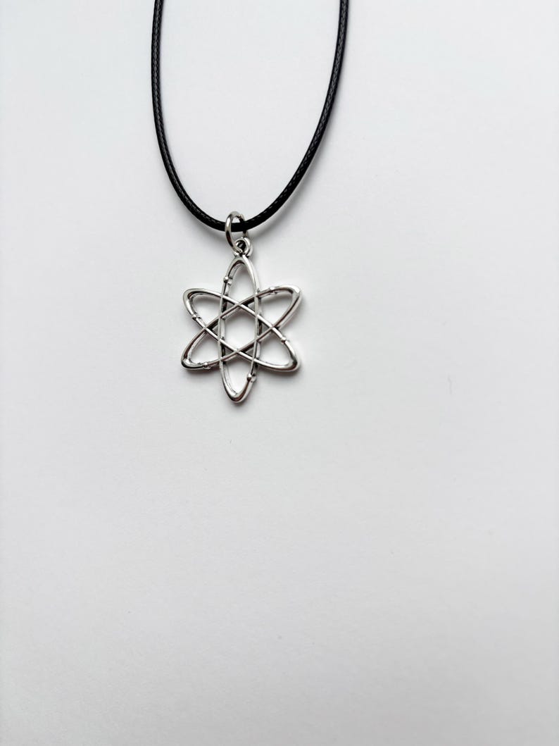 以下が含まれることがあります： 六芒星のデザインが特徴の、シルバーカラーのペンダントネックレス。ペンダントは黒いコードで吊り下げられています。ネックレスは白い背景に表示されています。