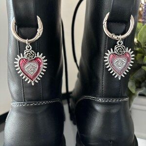 May include: A pair of black leather boots with silver heart-shaped charms. Each charm features a red and pink eye design.