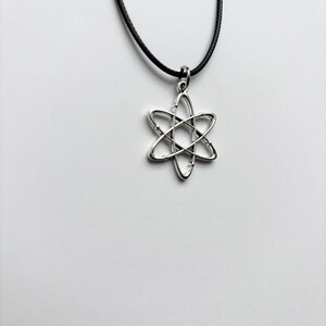 以下が含まれることがあります： 六芒星のデザインのシルバーカラーのペンダントネックレス。ペンダントは黒いコードから吊り下げられています。ネックレスは白い背景に表示されています。