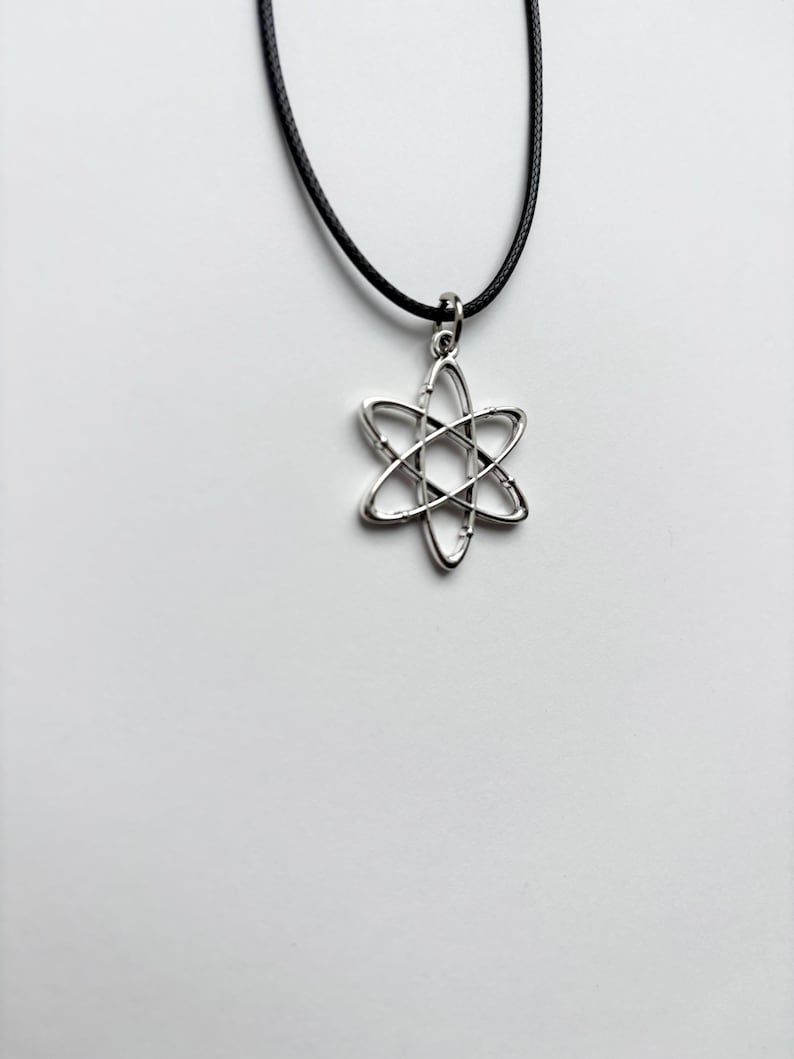 以下が含まれることがあります： 六芒星のデザインのシルバーカラーのペンダントネックレス。ペンダントは黒いコードから吊り下げられています。ネックレスは白い背景に表示されています。