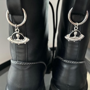 May include: A pair of black leather boots with silver charms. The charms are shaped like a UFO with an alien inside and the text "I want to believe".