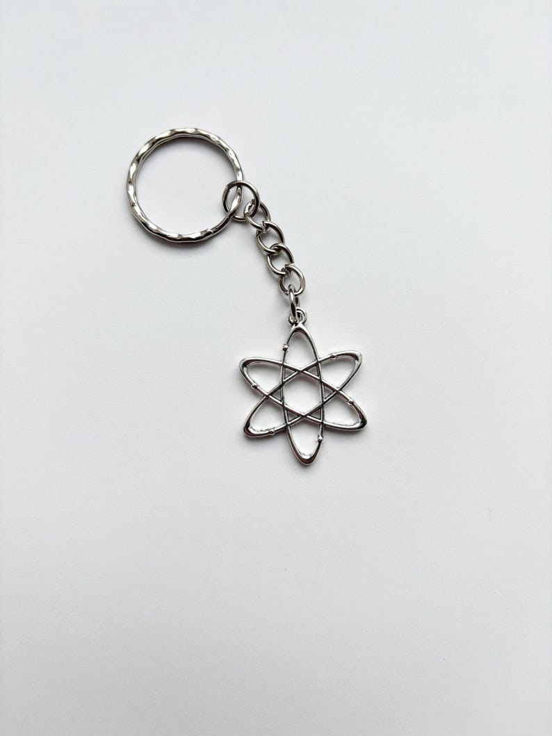 Może przedstawiać: Srebrny brelok do kluczy z sześcioramiennym wzorem gwiazdy, połączony z łańcuchem i teksturowanym k&oacute;łkiem na klucze. Brelok wykonany jest z błyszczącego metalu na gładkim białym tle.