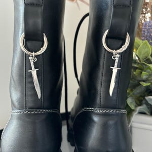 May include: Black leather boots with a silver dagger charm attached to each boot.