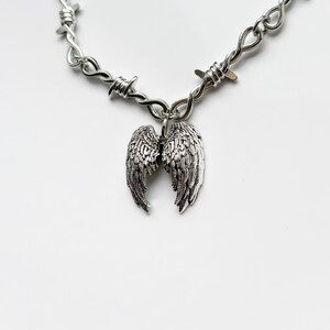 May include: A silver necklace with a barbed wire chain and a pendant of detailed angel wings. The jewellery is shown against a white background.