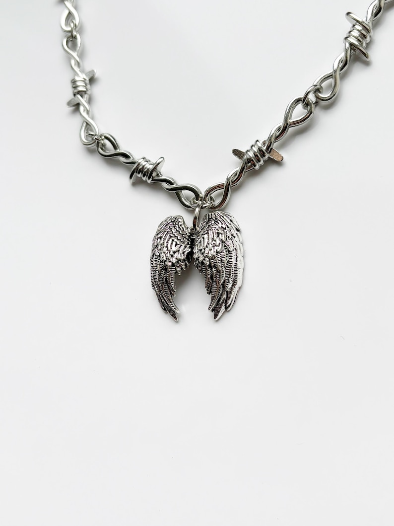 May include: A silver necklace with a barbed wire chain and a pendant of detailed angel wings. The jewellery is shown against a white background.