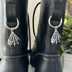 May include: Pair of black leather boots with silver spider web and spider charms attached to the laces.