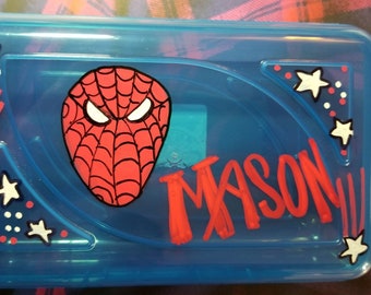 May include: Blue plastic pencil box featuring a red and black Spider-Man mask design. The name "MASON!!!" is written in red. White stars and red lines decorate the corners of the box.
