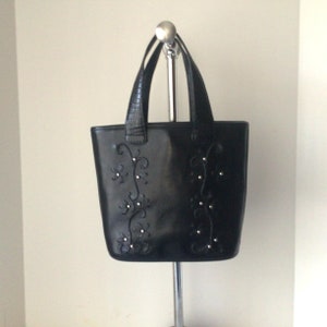 May include: Black leather tote bag with a floral design and silver embellishments.