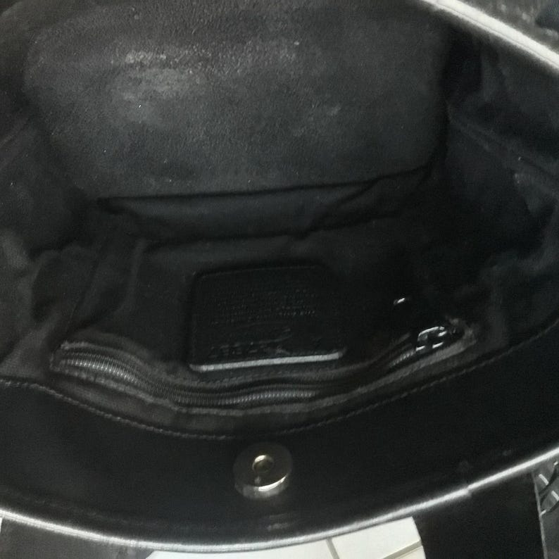 May include: Inside view of a black leather tote bag with a zippered pocket and a Coach brand label.