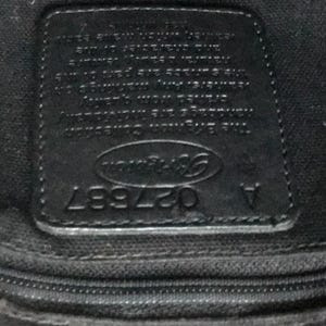 May include: Close-up of a black leather tag with the text "Coach" in a white oval and the number "027997" below it.