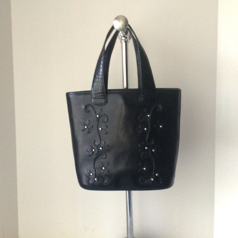 May include: Black leather tote bag with a floral design and silver embellishments.