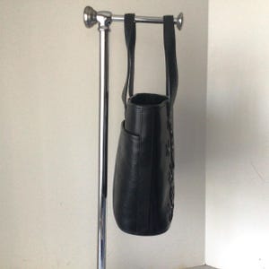 May include: Black leather tote bag with a floral design and silver accents. The bag has two top handles and a zipper closure.