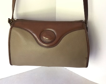 May include: A brown and beige leather shoulder bag with a brown leather flap and a metal buckle. The bag has a zipper closure and a long strap.