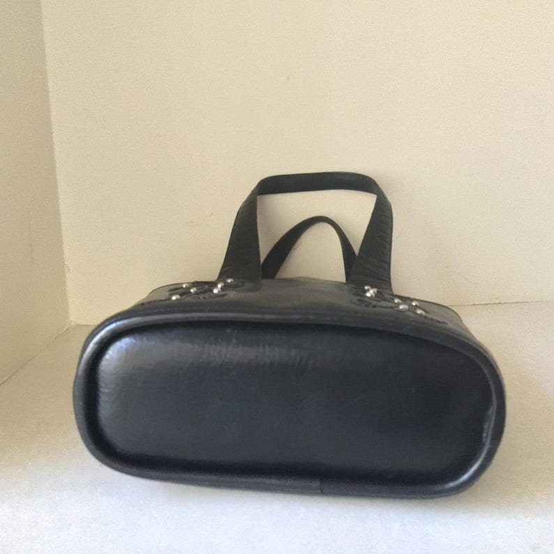 May include: Black leather tote bag with silver studs. The bag has a rounded bottom and two top handles.