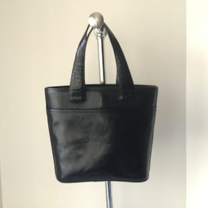 May include: A black leather tote bag with a top handle and a structured shape.