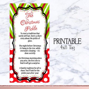 Op de afbeelding: Een printbaar Christmas Pickle-label met een rood, groen en wit ontwerp. Het label bevat de tekst "The Christmas Pickle" en een kort verhaal over de traditie. Het label is 10,16 x 20,32 cm groot.