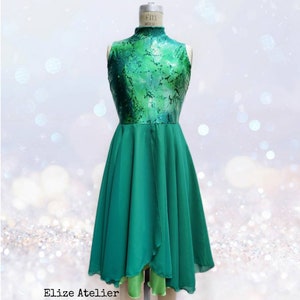 Puede incluir: Un vestido de baile verde sin mangas con cuello alto y un corpi&ntilde;o verde brillante. La falda es de gasa fluida y en capas con un dobladillo alto-bajo. El vestido est&aacute; en un maniqu&iacute; sobre un fondo brillante.
