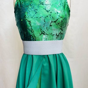 Puede incluir: Un leotardo verde sin mangas con cuello alto y un dise&ntilde;o estampado verde y blanco. Una banda el&aacute;stica blanca se lleva sobre el leotardo. Una falda larga verde con una abertura en la parte delantera se lleva sobre el leotardo y la banda.