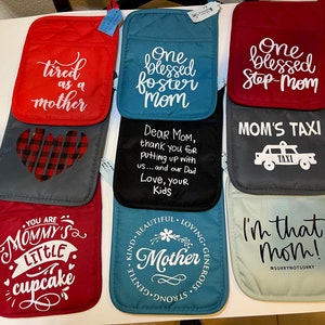 Puede incluir: Diez agarraderas diferentes con diversos lemas y diseños. Las agarraderas son rojas, azules, grises y azul claro. Algunos de los lemas incluyen "Cansada como una madre", "Una madre adoptiva bendecida", "Una madrastra bendecida", "Taxi de mamá", "Eres el pequeño cupcake de mamá", "Madre amable, hermosa, cariñosa, gentil, fuerte, generosa", y "¡Soy esa mamá! #LoSientoNoLoSiento".
