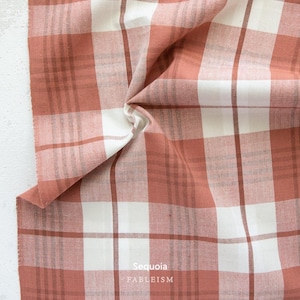 a close-up view of a fabric with a plaid pattern, featuring a mix of red and white colors. The fabric appears to be folded or crumpled, giving it a textured and cozy appearance.