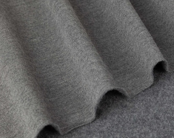 Op de afbeelding: Close-up van grijze stof met zichtbare textuur en plooien. Het materiaal lijkt zacht en drapeert natuurlijk, met subtiele kleurvariaties. Het oppervlak van de stof heeft een licht wazig uiterlijk.