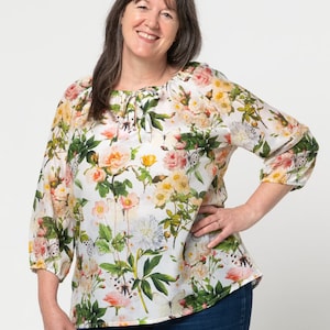 May include: A white blouse with a floral print featuring butterflies, roses, and other flowers. The blouse has a gathered neckline and 3/4 sleeves.
