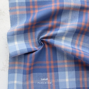 a close-up view of a fabric with a plaid pattern in shades of blue, orange, and white. The fabric appears to be folded or crumpled, creating a textured and visually interesting surface.