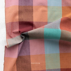May include: A close-up shot of a fabric with a large plaid design. The fabric is composed of squares in shades of pink, orange, brown, teal, and blue. The word "FABLEISM" is printed in white on the lower right corner.