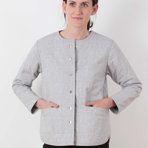 May include: A gray quilted jacket with a button-up front and two patch pockets. The jacket has a round neckline and long sleeves.