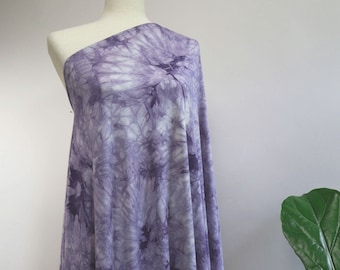 May include: Purple tie-dye fabric on a white dress form. The fabric has a swirling pattern with shades of light and dark purple.