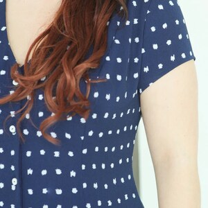 May include: A navy blue dress with a white polka dot pattern. The dress has a v-neckline and short sleeves.