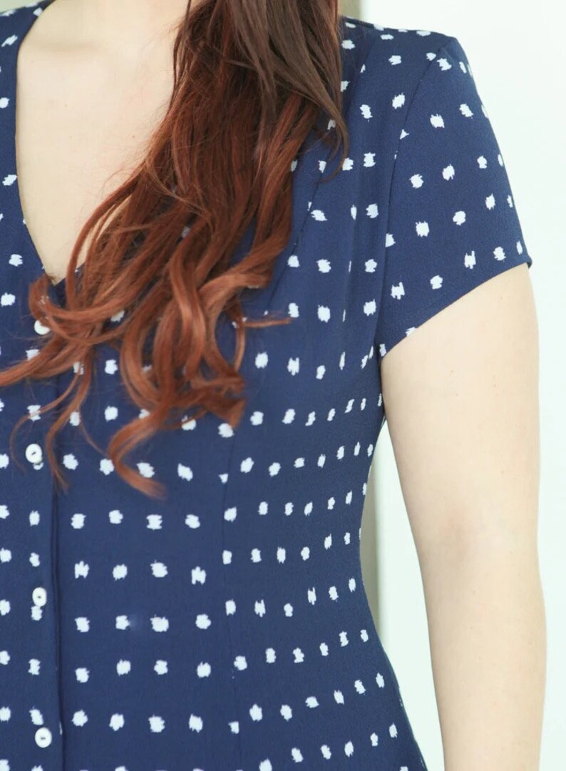 May include: A navy blue dress with a white polka dot pattern. The dress has a v-neckline and short sleeves.