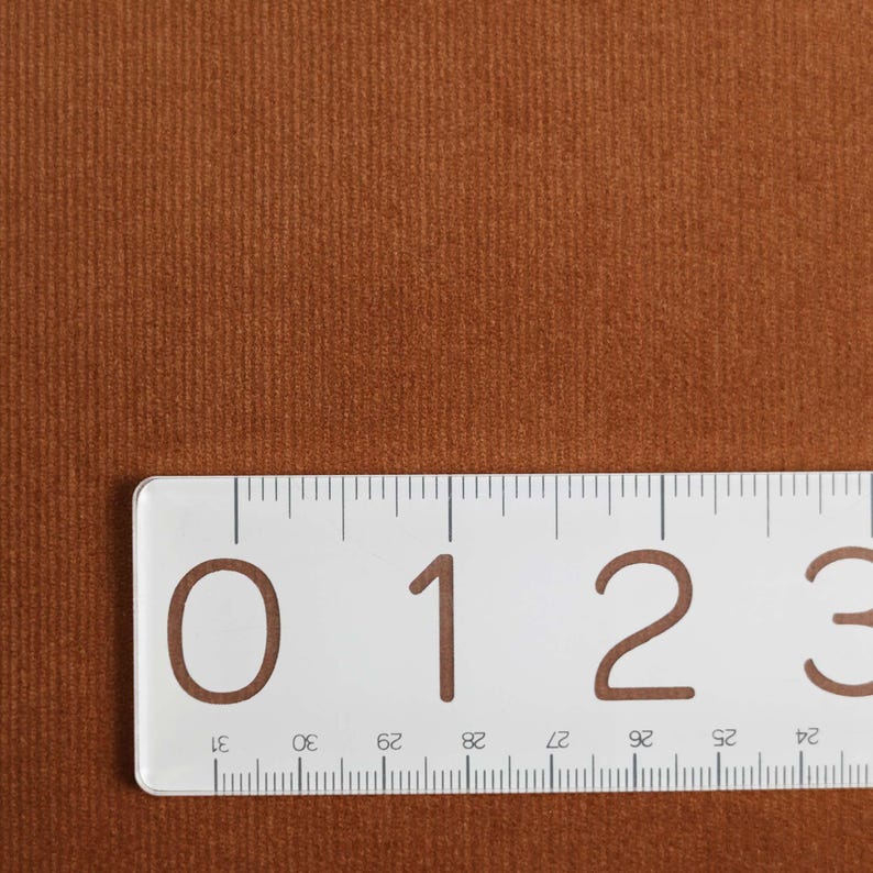 May include: Close-up of a brown corduroy fabric with a ruler showing the measurement of 3 inches.