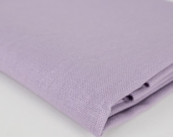 May include: Folded lavender-colored linen fabric. The fabric has a textured weave and appears soft. The color is a light, muted purple, and the fabric is neatly folded, showing the edges and layers.