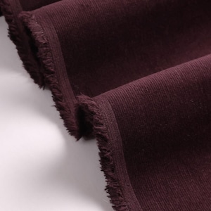 May include: Close-up of a deep burgundy corduroy fabric with a frayed edge.