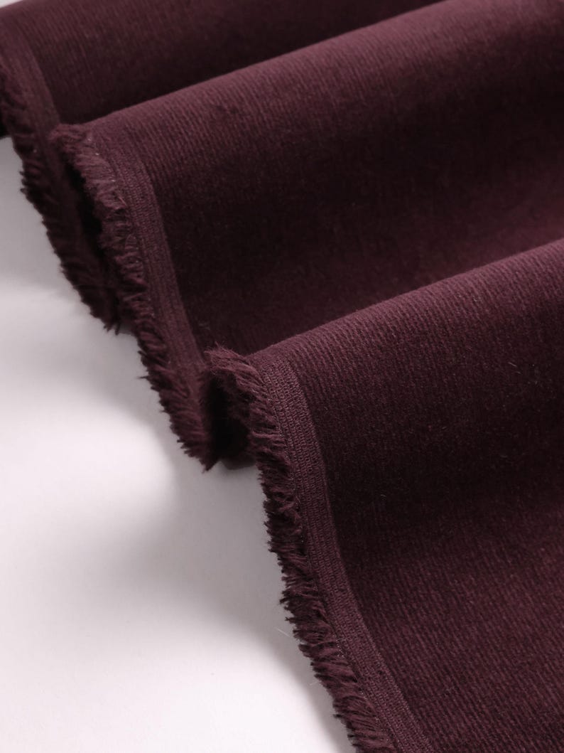 May include: Close-up of a deep burgundy corduroy fabric with a frayed edge.