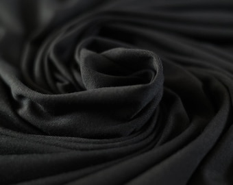 May include: Close-up of a black fabric with a soft, smooth texture. The fabric is draped and folded, creating a sense of depth and dimension.