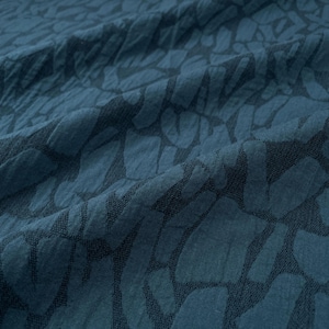 May include: Close-up of a teal fabric with a textured pattern. The pattern consists of dark teal shapes resembling irregular rectangles. The fabric is slightly wrinkled, creating shadows and depth. The overall effect is a modern, abstract design.