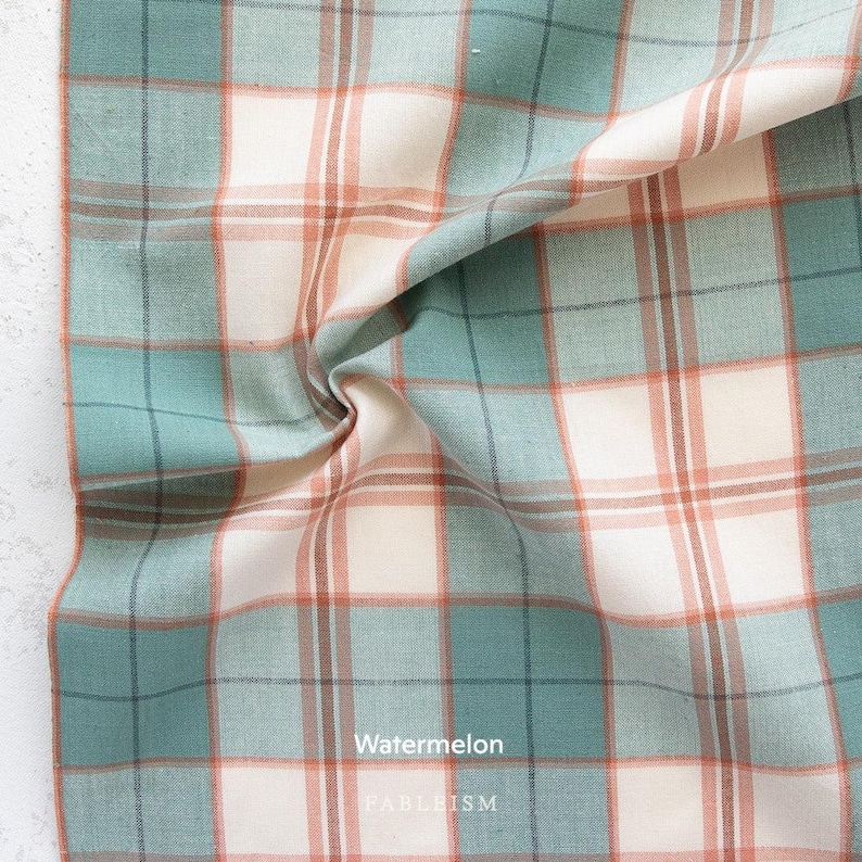 a close-up view of a fabric with a plaid pattern in shades of blue, green, and orange. The fabric appears to be made of cotton and has a crinkled texture.