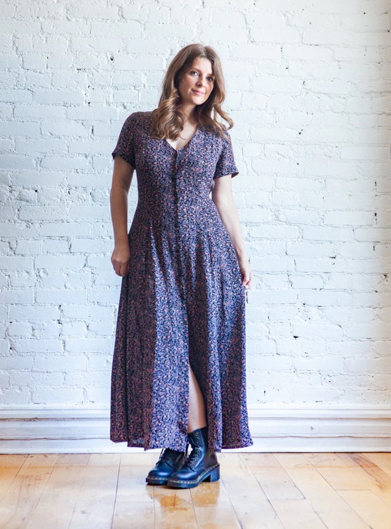 May include: A woman wearing a long, floral print dress with a button-up front and short sleeves. She is wearing black combat boots.