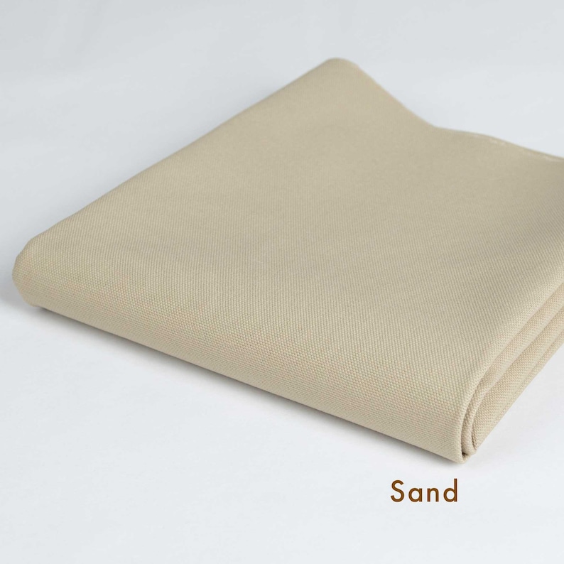 May include: A folded piece of beige fabric with a smooth texture. The fabric is labeled "Sand".