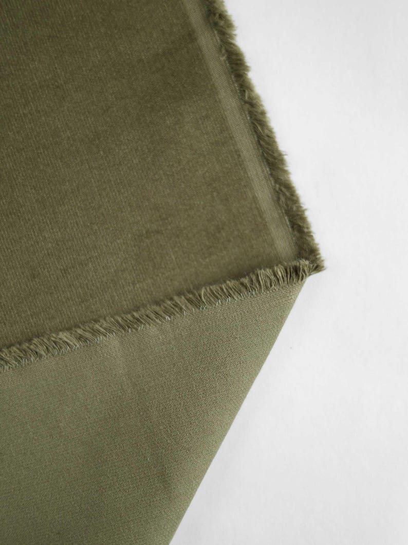 May include: Close-up of a piece of green corduroy fabric with a frayed edge.