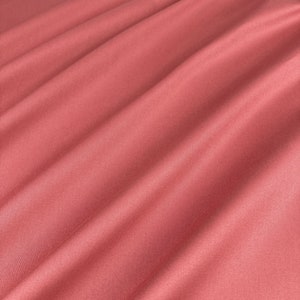 Könnte beinhalten: Nahaufnahme eines glatten, korallenrosa Stoffes mit weichen Falten und Knittern.