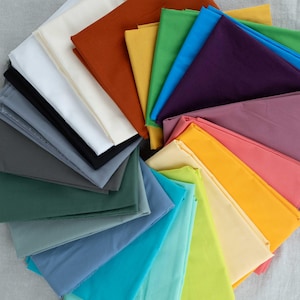 May include: A selection of folded fabric swatches in various colours, including white, black, grey, green, blue, yellow, orange, and purple. The swatches are arranged in a circular pattern, displaying the different shades.