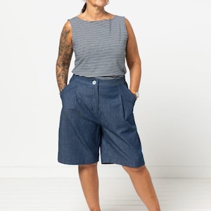 May include: A woman wearing a sleeveless navy and white striped top and denim blue shorts. The shorts have pleats and pockets. She is wearing silver platform shoes. The outfit is casual and stylish.