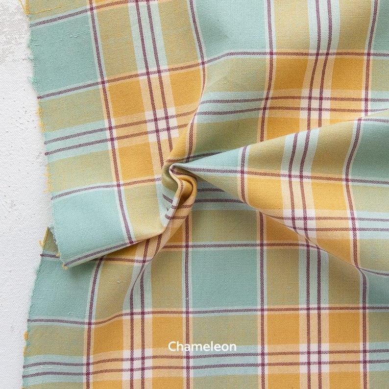 a close-up view of a fabric with a plaid pattern in shades of green, yellow, and orange. The fabric appears to be folded or crumpled, creating a textured and visually interesting surface.